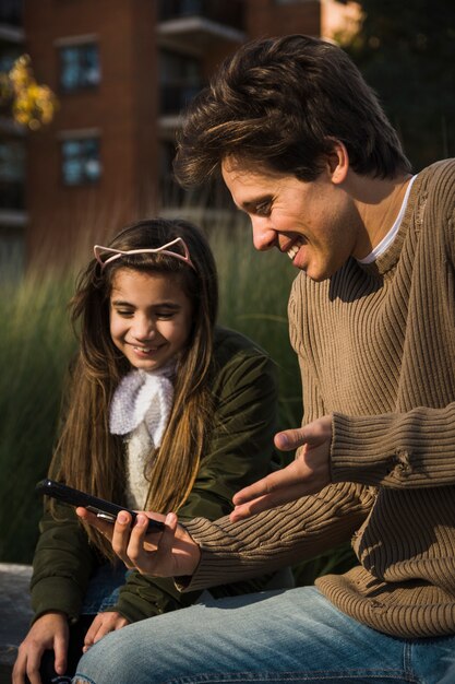 Primer plano de sonrientes padre e hija mirando teléfono inteligente