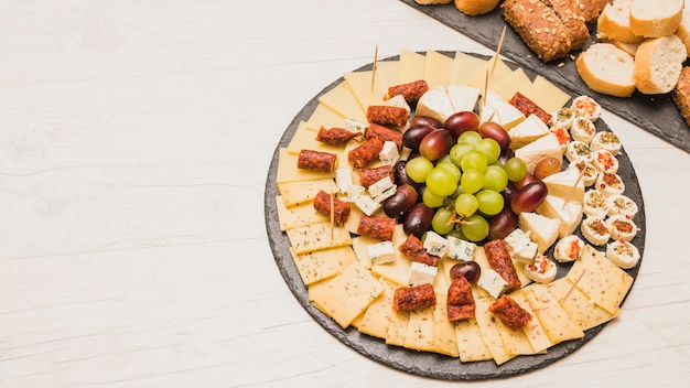 Primer plano de una tabla de quesos con uvas y salchichas ahumadas en tablero de pizarra