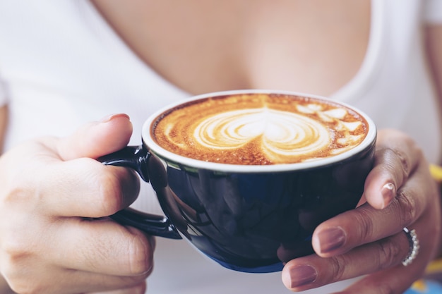 Foto gratuita primer plano de una taza de arte latte de café en mano de mujer en cafetería cafetería