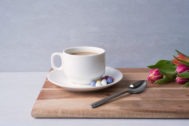 Primer plano de una taza de café caliente con leche en el tablero cerca de un ramo de flores bajo las luces