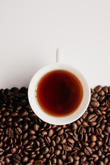 Primer plano de una taza de café con granos de café sobre un fondo blanco.