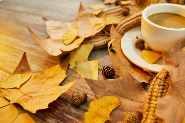 Primer plano de una taza de café y hojas de otoño sobre la superficie de madera