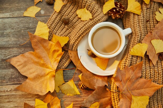 Primer plano de una taza de café y hojas de otoño sobre la superficie de madera