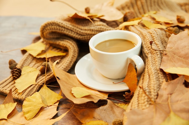 Primer plano de una taza de café y hojas de otoño sobre la superficie de madera