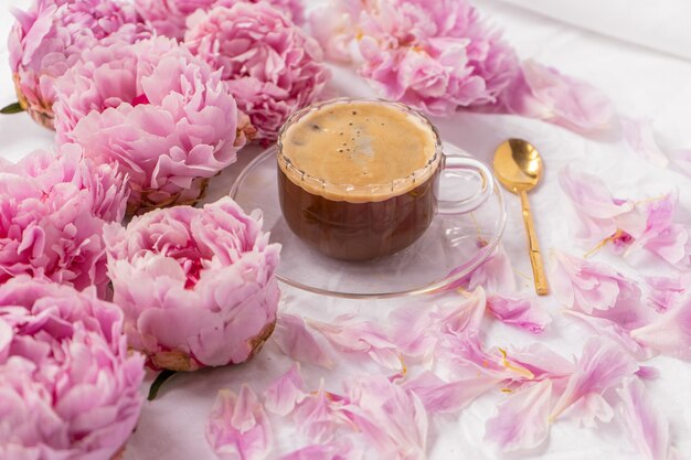 Primer plano de una taza de café instantáneo en un platillo sobre la mesa con peonías rosas en él