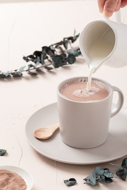 Primer plano de una taza de café con leche y algunas decoraciones sobre una mesa blanca