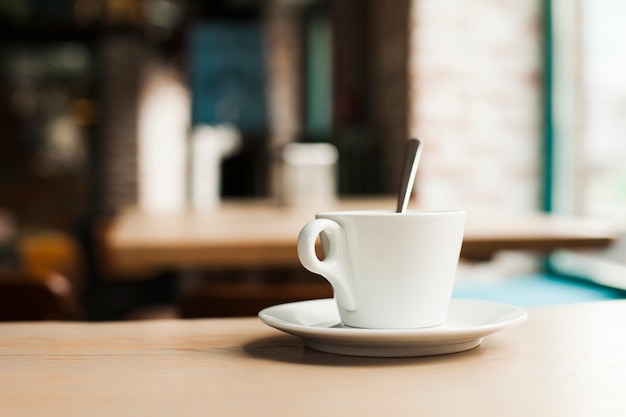 Primer plano de la taza de café con el platillo en la mesa de madera en la cafetería