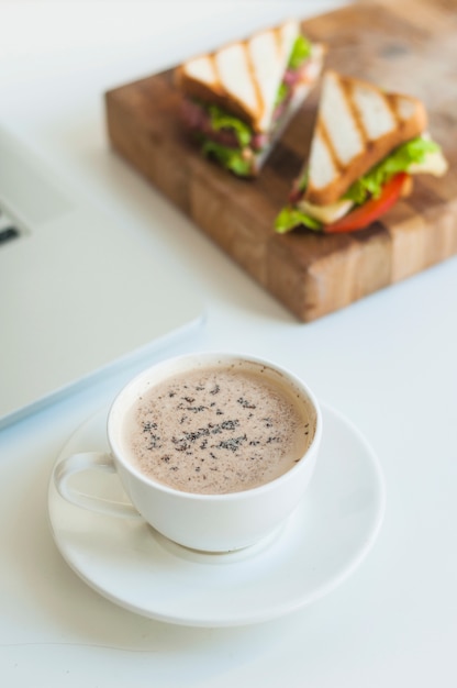 Primer plano de la taza de café con sándwiches en tabla de cortar de madera