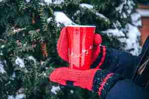 Foto gratuita primer plano de una taza térmica roja en las manos con mitones rojos