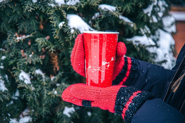 Primer plano de una taza térmica roja en las manos con mitones rojos