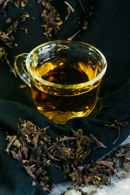 Primer plano de té de hierbas en una taza de vidrio con hojas de té secas