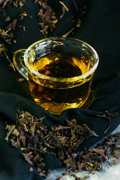 Primer plano de té de hierbas en una taza de vidrio con hojas de té secas