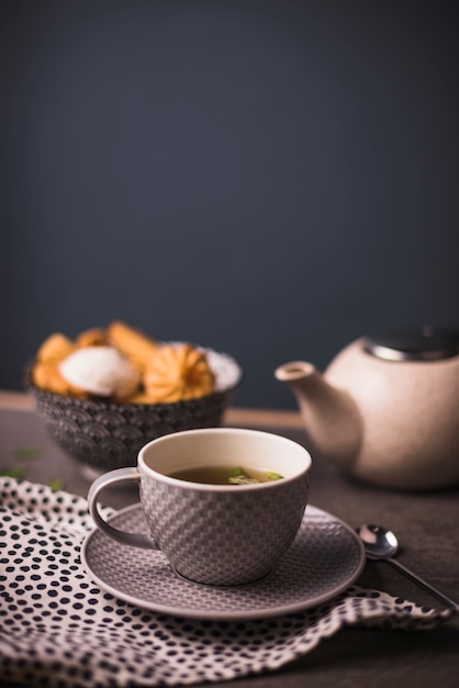 Primer plano de té de hierbas con tazón de galletas y tetera en el fondo