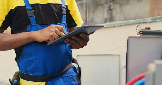 Primer plano de un técnico hábil comisionado para el mantenimiento de rutina del sistema HVAC externo, en busca de problemas de refrigerante. Mecánico meticuloso haciendo inspección de aire acondicionado, escribiendo datos en tableta