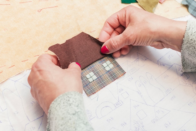 Primer plano de la tela de costura de la mano de una mujer en forma de casa sobre papel