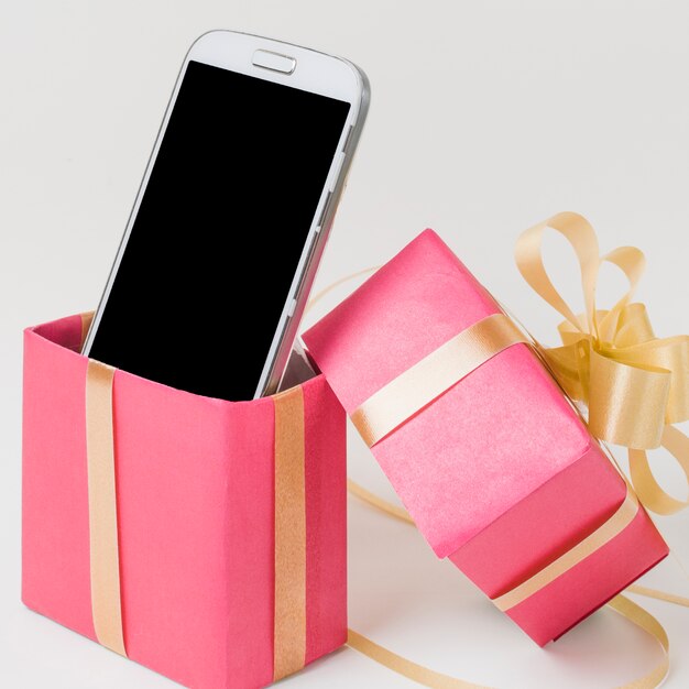 Primer plano de un teléfono celular en caja de regalo rosa decorada contra superficie blanca