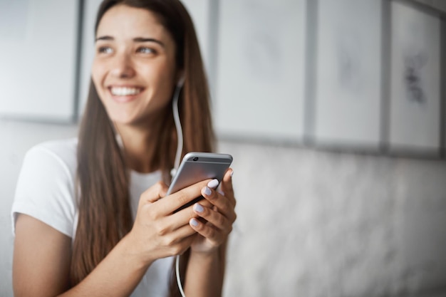 Primer plano de un teléfono inteligente en manos femeninas Chica escuchando música en línea riendo y sonriendo