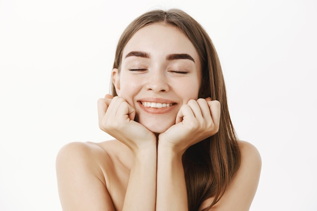 Primer plano de una tierna mujer bonita soñadora y femenina con cabello castaño apoyando la cabeza en las manos con los ojos cerrados y una dulce sonrisa encantada recordando o imaginando un buen momento