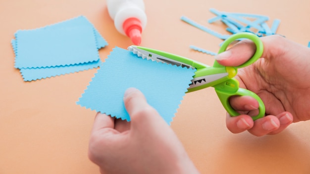 Primer plano de una tijera cortando el papel azul sobre fondo coloreado