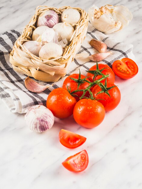 Primer plano de tomates jugosos frescos; cebollas; dientes de ajo y tela sobre fondo de mármol