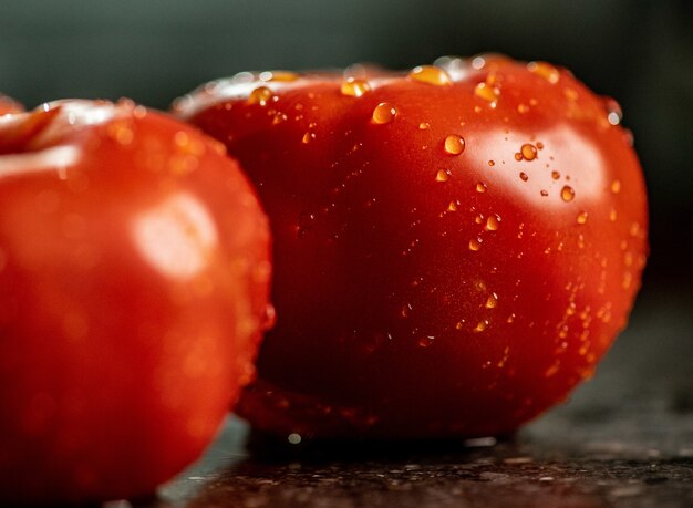 Primer plano de tomates maduros frescos con gotas de agua sobre una superficie de encimera de cocina de granito negro