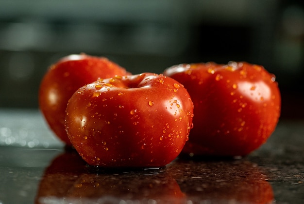 Primer plano de tomates maduros frescos con gotas de agua sobre una superficie de encimera de cocina de granito negro