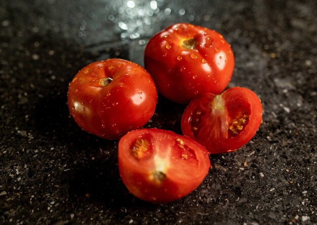 Primer plano de tomates maduros frescos con gotas de agua sobre una superficie de encimera de cocina de granito negro