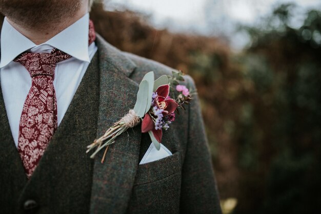 Primer plano de un traje de novio con flores y corbata estampada roja con árboles en el fondo