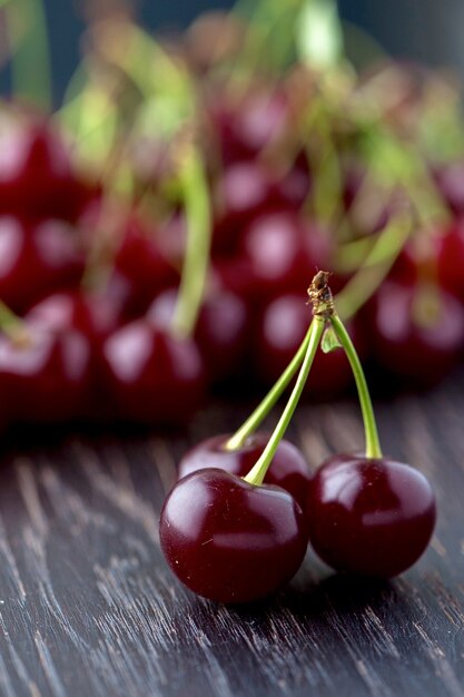 Primer plano de tres cerezas granate configuradas verticalmente sobre una superficie de madera