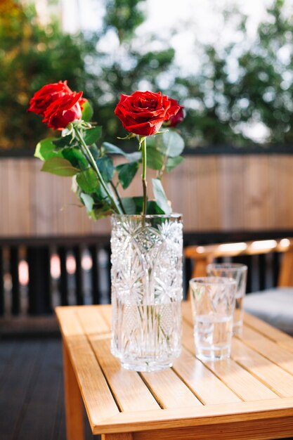 Primer plano de tres hermosas rosas rojas en florero de vidrio sobre la mesa de madera