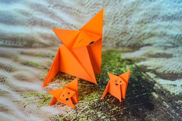 Primer plano de tres origamis de papel naranja con caras dibujadas sobre ellos sobre una superficie estampada