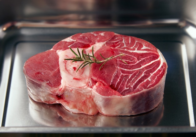 Primer plano de un trozo de filete de pierna angus con hoja de romero en la parte superior. Dentro de sartén de acero y listo para cocinar.