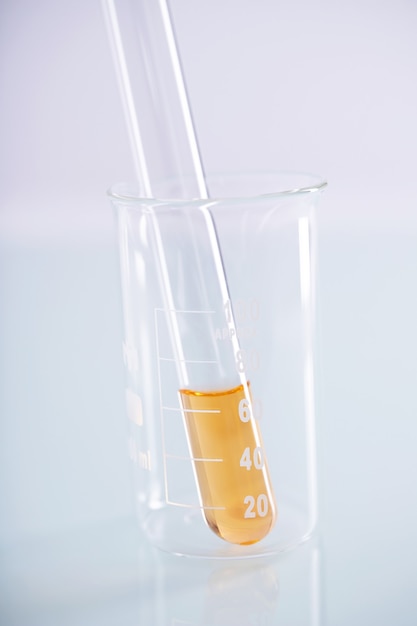 Primer plano de un tubo de ensayo con líquido amarillo dentro de un vaso de precipitados sobre una superficie blanca