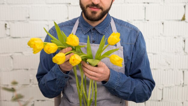 Primer plano de turista masculino sosteniendo los tulipanes amarillos en la mano de pie contra la pared blanca