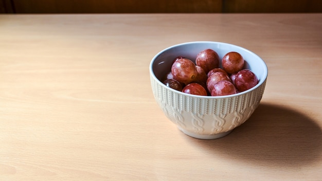 Primer plano de uvas en un tazón pequeño sobre una mesa de madera