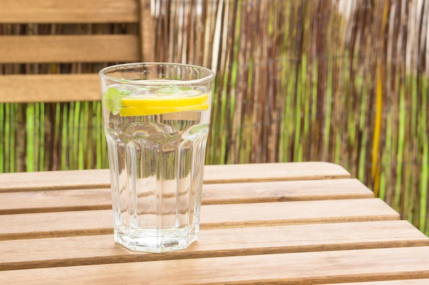 Primer plano de un vaso de agua con limón y menta en un banco de madera