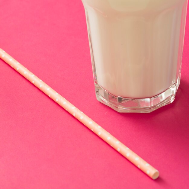 Primer plano de vaso de leche con pajita sobre fondo rosa