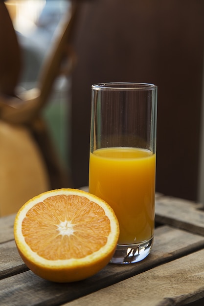 Primer plano de un vaso medio lleno de jugo de naranja y una naranja en rodajas en una caja de madera