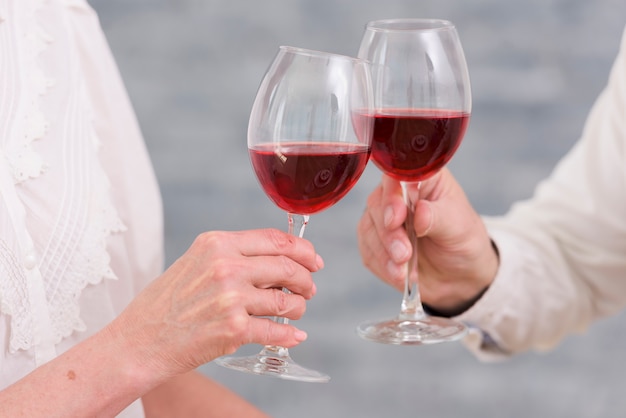 Foto gratuita primer plano de los vasos tintineantes de vino de una pareja juntos contra el fondo borroso