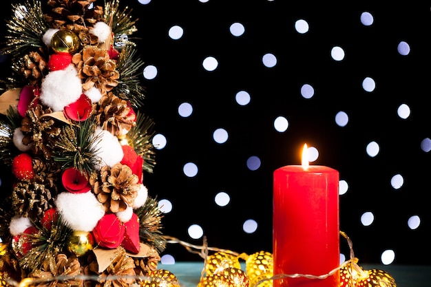 Primer plano de una vela encendida junto al mini árbol de navidad en la luz festiva del bokeh. Decoración y vacaciones. Temporada y año nuevo