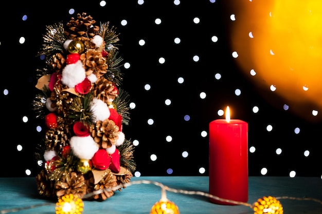 Foto gratuita primer plano de una vela encendida junto al mini árbol de navidad en la luz festiva del bokeh. decoración y vacaciones. temporada y año nuevo