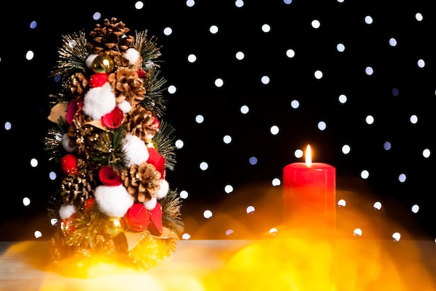 Primer plano de una vela encendida junto al mini árbol de navidad en la luz festiva del bokeh. Decoración y vacaciones. Temporada y año nuevo