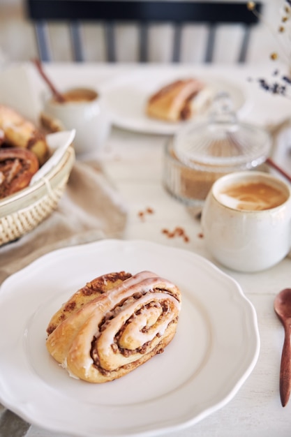 Primer plano vertical de deliciosos caracoles de nuez con café capuchino sobre la mesa de madera blanca