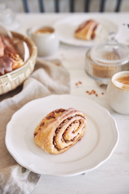 Primer plano vertical de deliciosos caracoles de nuez con café capuchino sobre la mesa de madera blanca