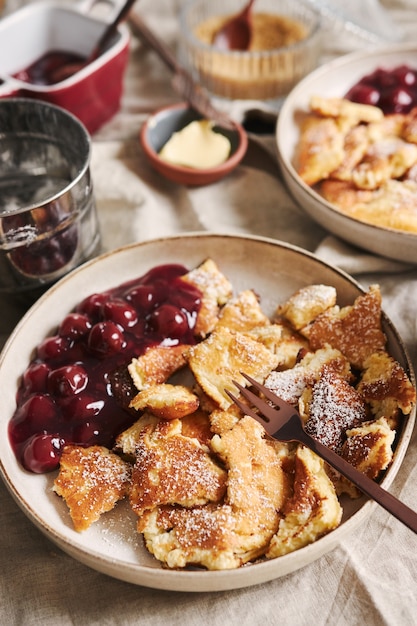 Primer plano vertical de deliciosos panqueques esponjosos con cereza y azúcar en polvo