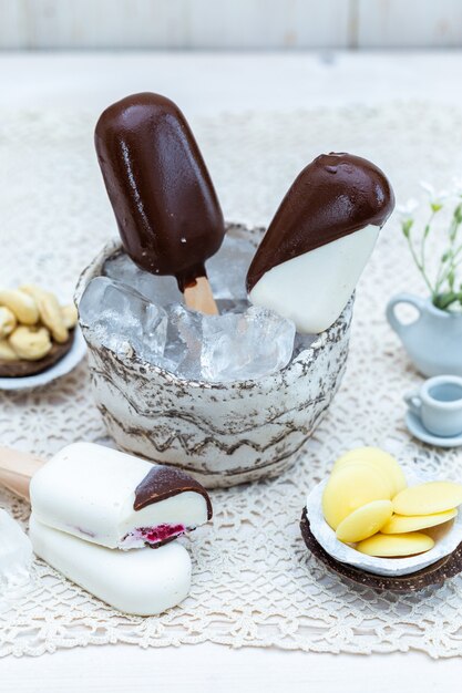 Primer plano vertical de helado vegano en palos en un recipiente con cubitos de hielo sobre una mesa