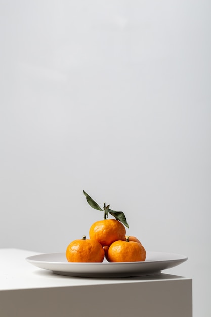 Primer plano vertical de mandarinas en un plato sobre la mesa bajo las luces sobre un fondo blanco.