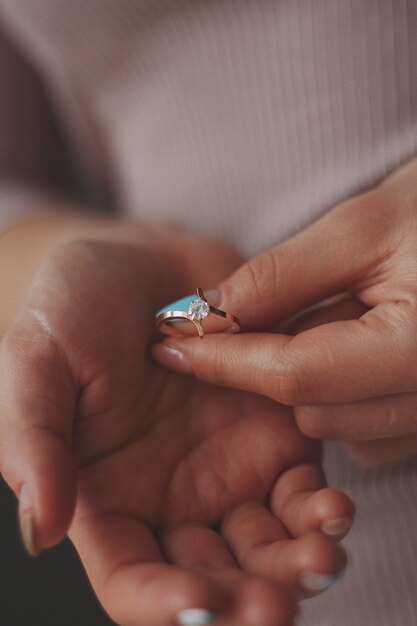 Primer plano vertical de una mujer sosteniendo un hermoso anillo de diamantes de oro