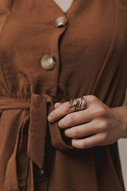 Primer plano vertical de una mujer vistiendo un vestido marrón y un anillo metálico en forma de hoja