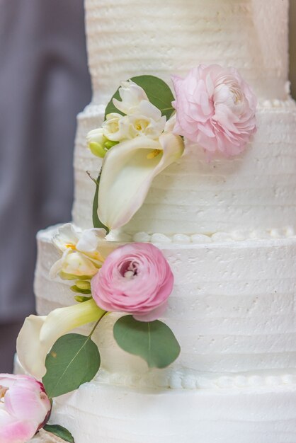 Primer plano vertical de un pastel de boda decorado con flores.